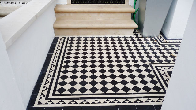 Black and White garden path tiles with border made up of different sized triangles lead to York stone steps with daisy grate ventilation grill.