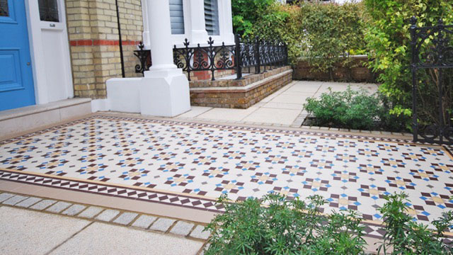 Large garden path of colourful geometric ceramic tiles, framed with sandstone paving.