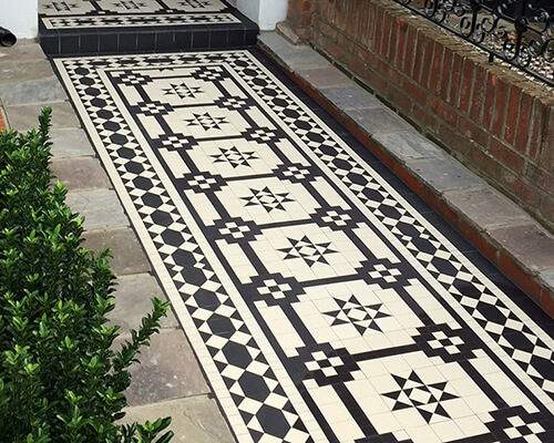 Black and White geometric mosaic path tiles framed by stone slabs. Decorative iron railings sit on top of a small red brick wall.