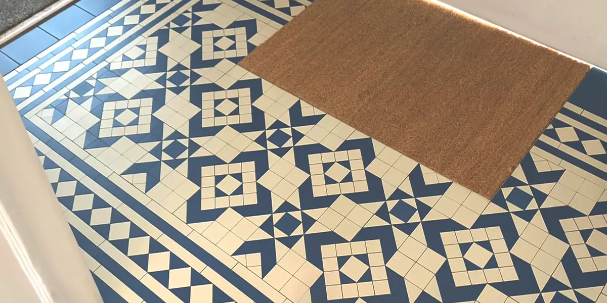 Blue and white geometric floor tiles in entrance hall. A coirmat is visible. Natural light is shining on the tiles to the left.