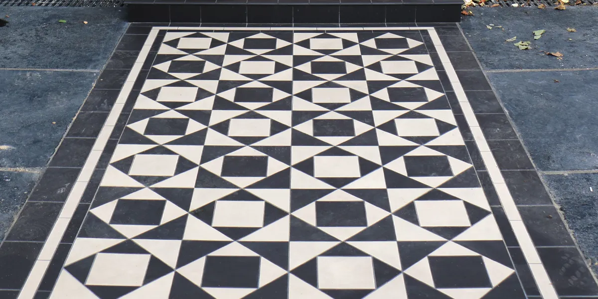 A bold geometric tiled pattern on entryway. Stone slabs are laid to the sides of the path.