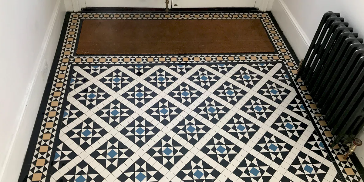 Victorian hall floor tiles fitted around a large brown coir mat. To the right a black cast-iron radiator.