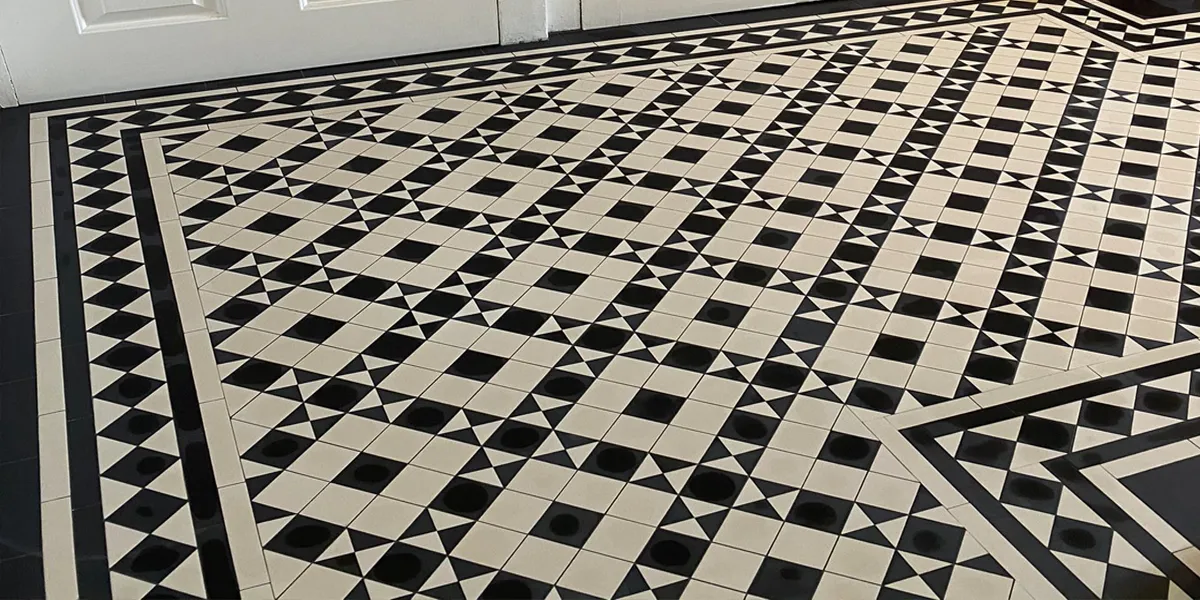 A Georgian or Victorian style mosaic tiled floor in an entrance hallway. The design uses small black and white squares and triangles in a trellis and dot pattern. A traditional border motif frames the tiled design at the perimeter of the entrance hall.