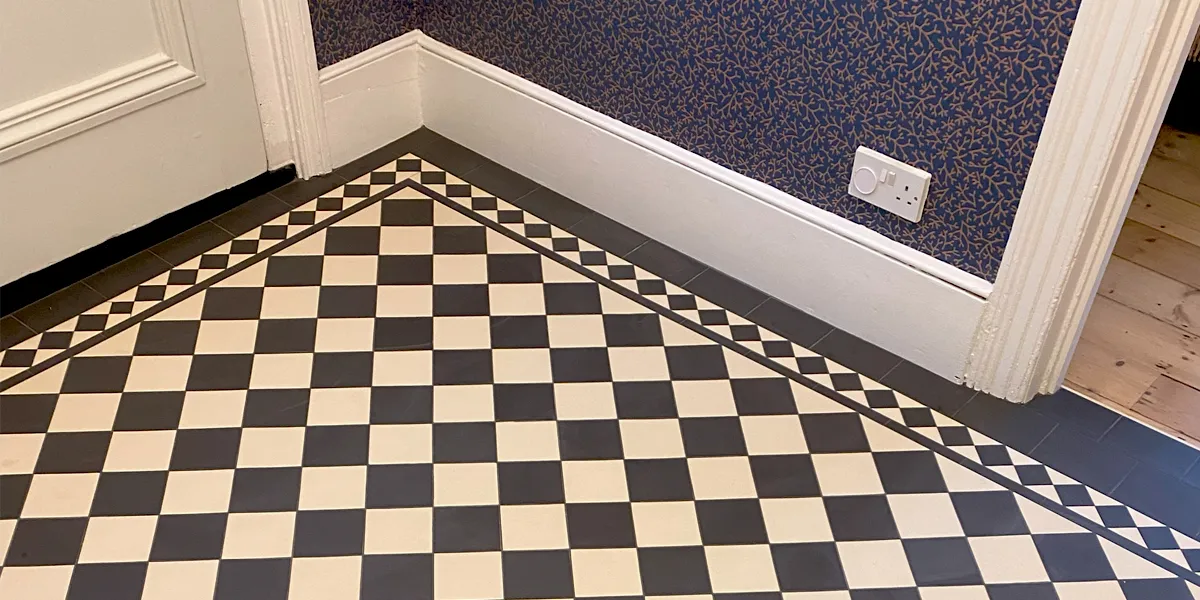 A Victorian chequerboard hallway in black and white. There is white gloss painted skirting, architraves and doors. An open door leads to a room with exposed  floorboards