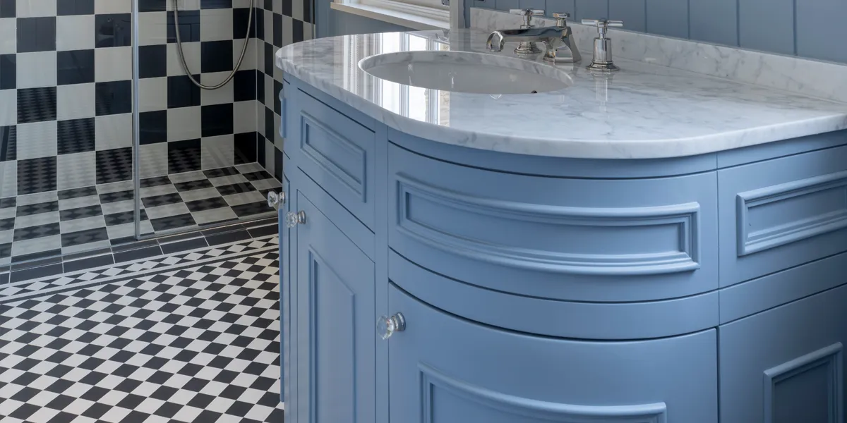 Black and white chess board tiles used on bathroom floor and inside shower cabin, alongside vanity unit painted blue with marble top.