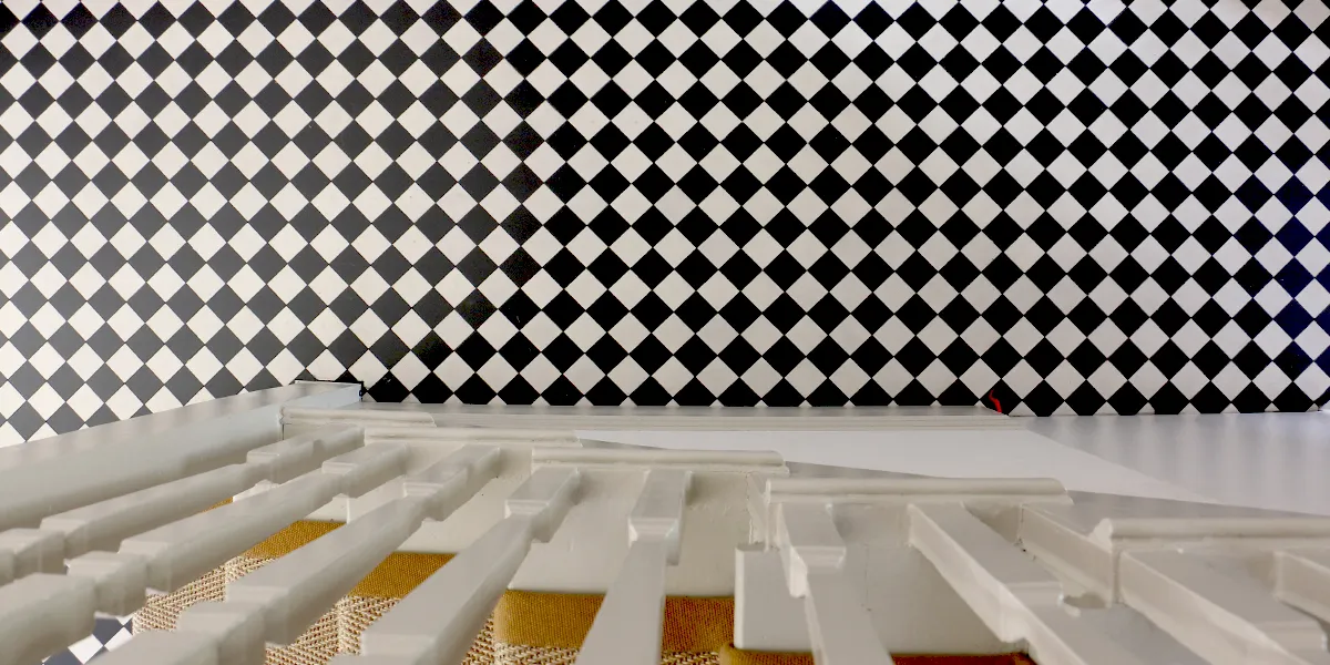 Birds-eye view, looking down from the side of a staircase, of a black and white chequerboard hallway floor.