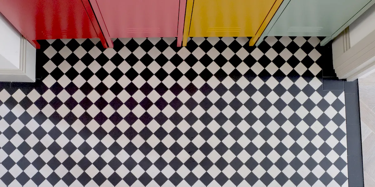 Birds-eye view of chequerboard hallway floor tiles alongside colourful metal cabinets.