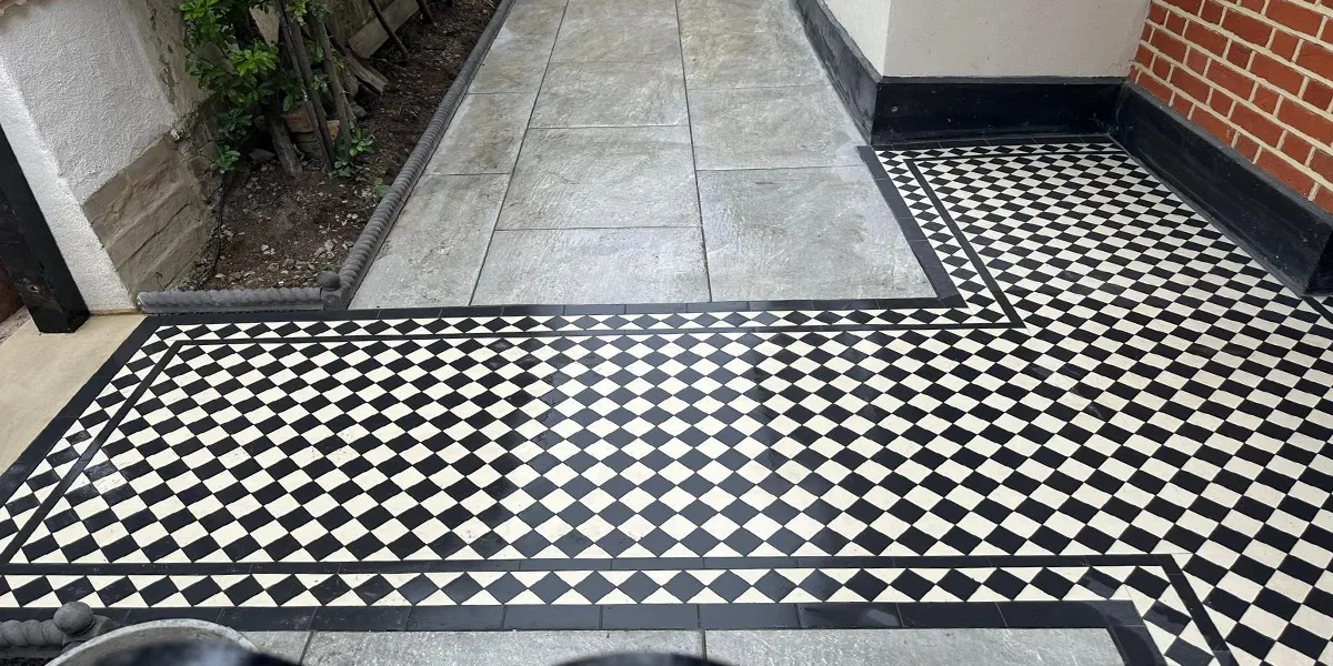 New installation of Victorian style black and white path tiles leading from stone tread at the gate to a porch area at the front of the red brick house. Stone slabs to the rest of the area.
