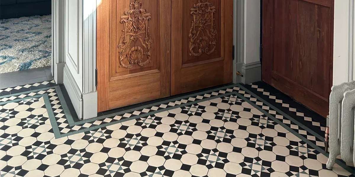 Black, white and green victorian hall floor tiles infront of carved wooden cupboard.