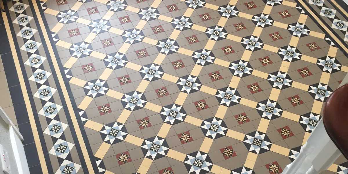 View from staircase looking down on decorative Victorian hall floor tiles. The mosaic design has a wide border pattern.