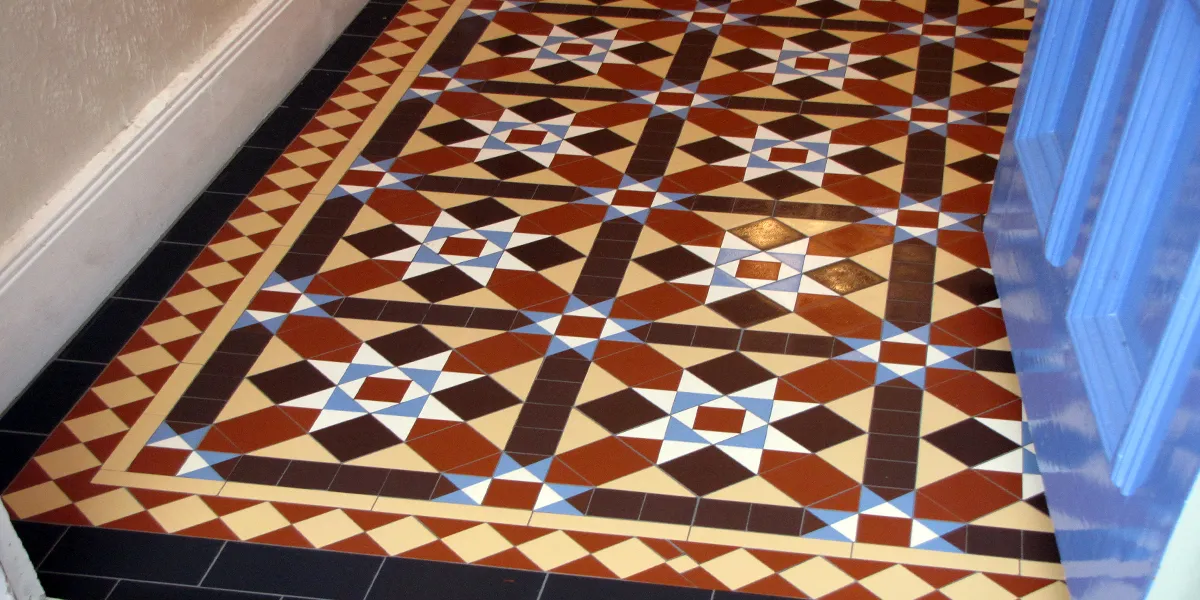 A multi-colour Victorian mosaic tiled hallway, with glossed skirting boards, and embossed wallpaper. To the right, the blue front door is pushed open.