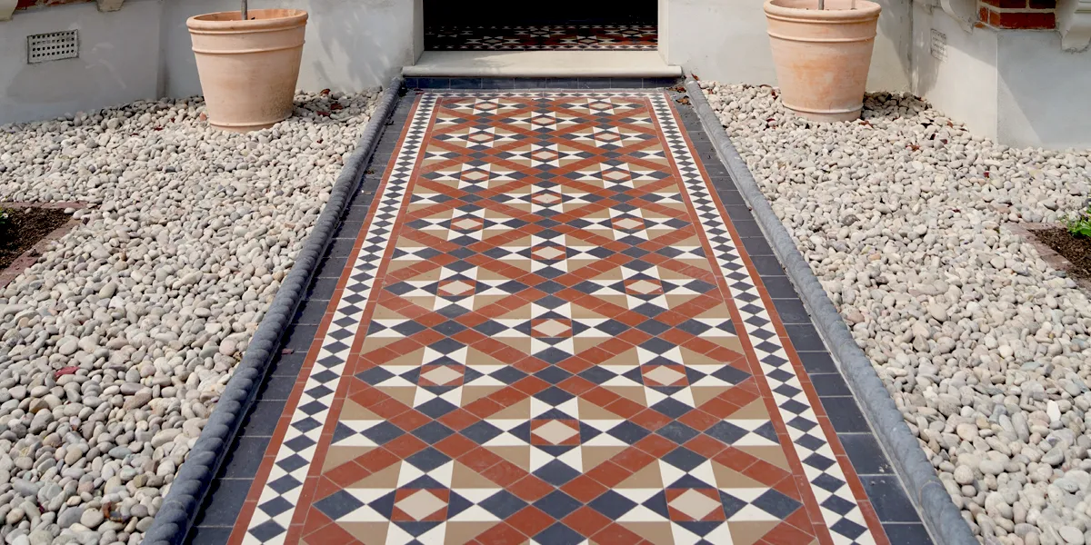Edwardian style red, black and brown path tiles with pebbles alongside.