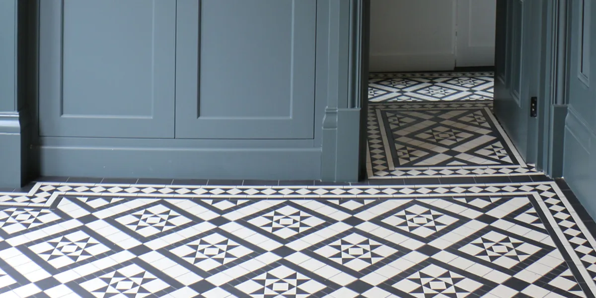 A black and white geometric mosaic floor tile pattern in a hall. The wooden wall panels, skirting, architraves and doors are colour-drenched in a blue-grey tone.