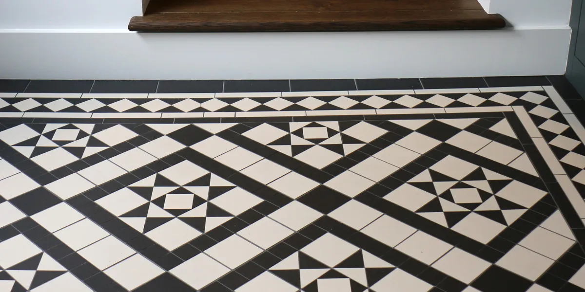 A black and white mosaic tile pattern in contrasting star and box motifs. The design is framed by a diamond border. A step to the rear rises to a dark-stained wood tread.