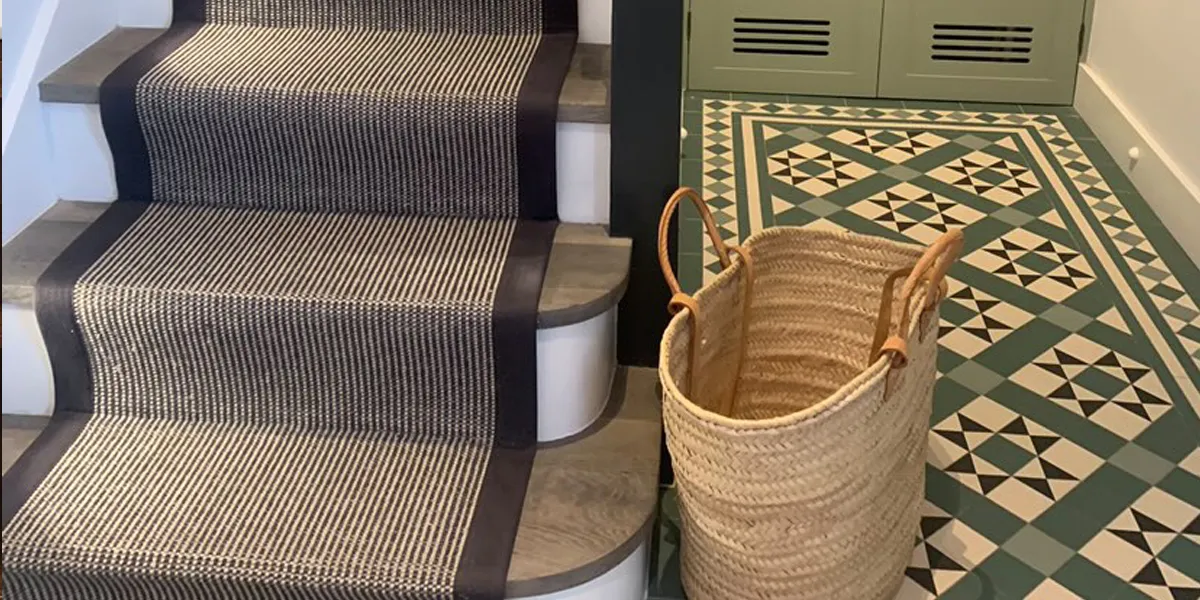 Green toned Victorian tile pattern in hallway alongside staircase with runner, and large basket.