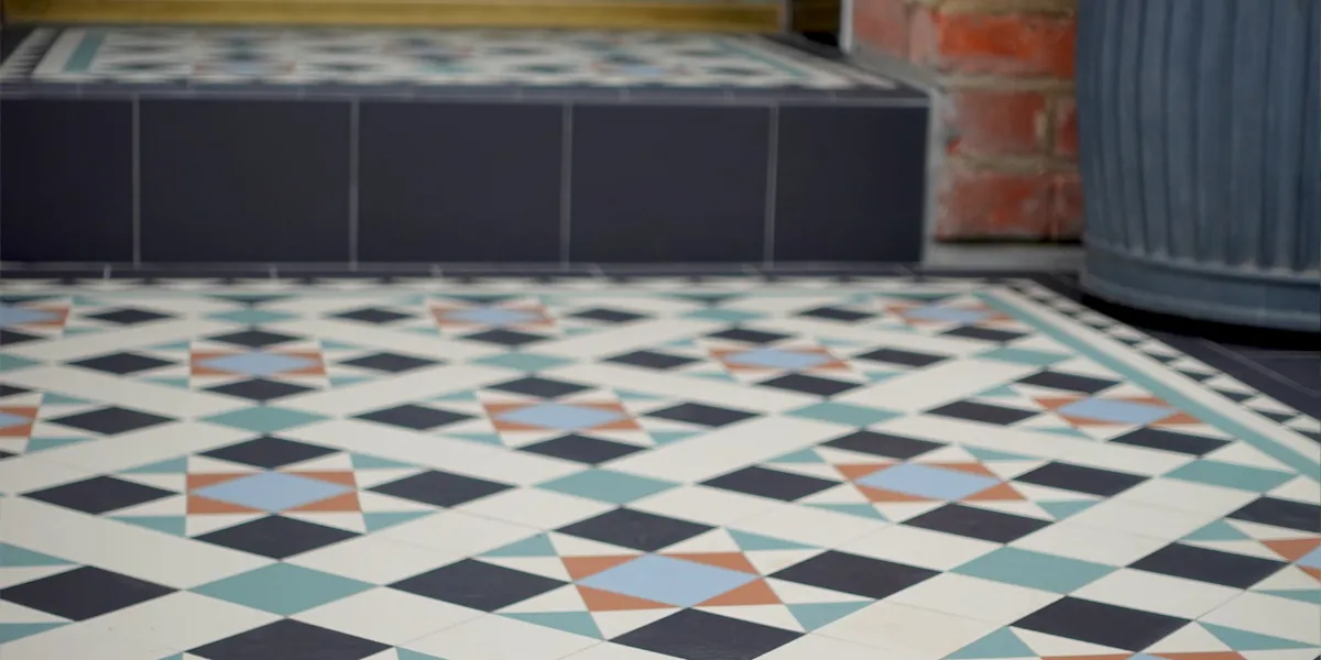 Close view of colourful Victorian mosaic path and porch tiles. The design contrasts black and white, with reds, blues and greens. The porch step has round edge tiles to the edge of the tread.