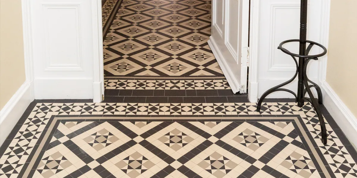 A Victorian star and box motif mosaic leads from a vestibule into the hall. The black, white and grey design is framed with a border of geometric mosaic stars. The base of a traditional free standing coat-rack is in the right-hand corner.