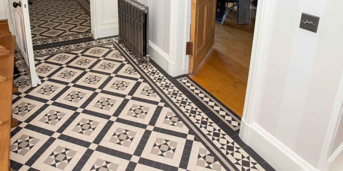 A black, white and grey tiled mosaic hallway floor, with a view to the vestibule, and through an open wooden door to the right,a livingroom with wooden floorboards.