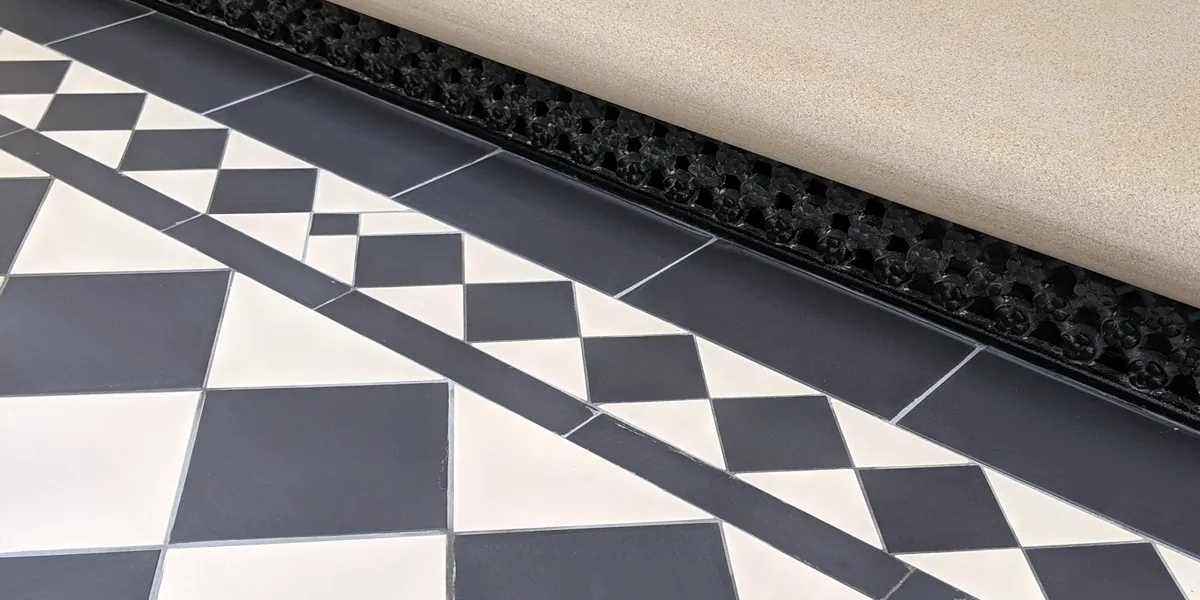 Close up view of a black and white path leading to a stone step tread. Beneath the step a traditional daisygrate ventilation grille.
