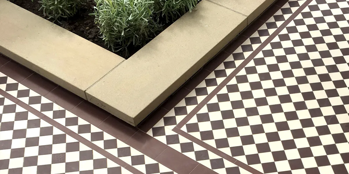 Brown and white chequered pathway tiles alongside a raised bed of lavender bushes framed with sandstone.
