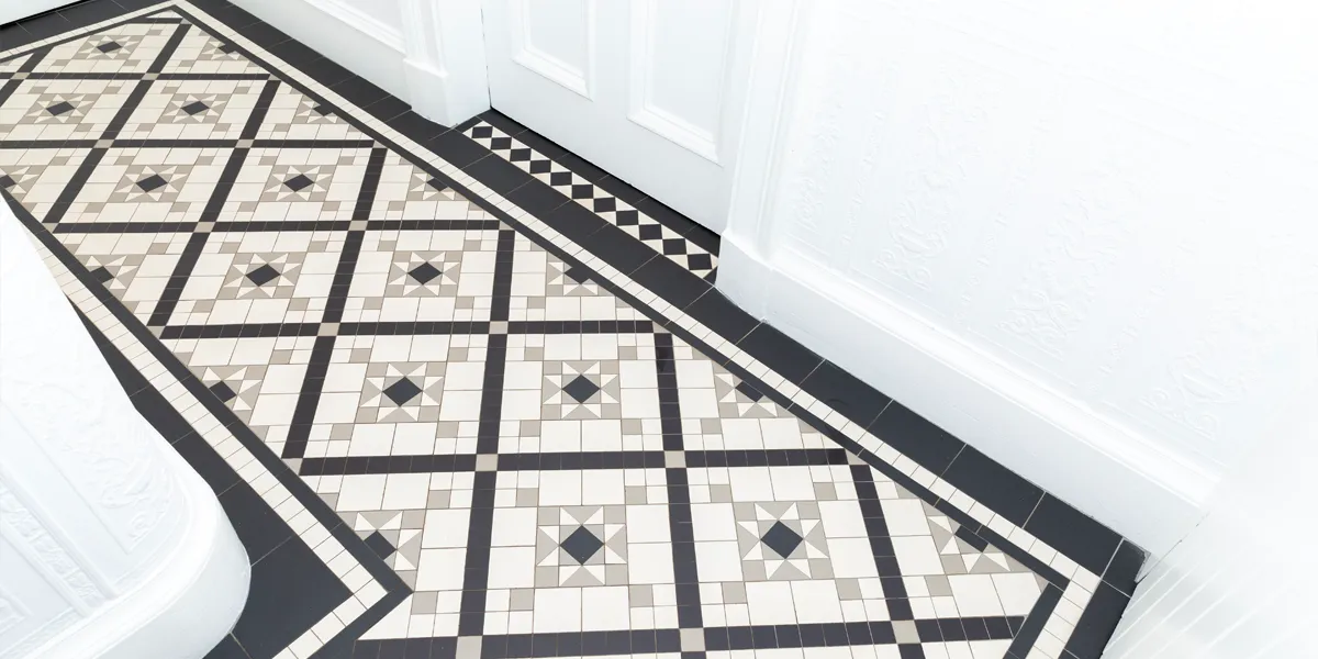 A black, white and grey, mosaic tiled hallway floor. The walls have a moulded relief wallpaper, and everything is painted white including the doors, architraves and skirting.