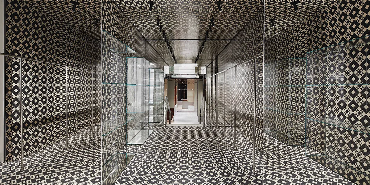 A Givenchy shop interior with a black and white Victorian mosaic tile pattern on the walls, floors and ceiling. The space is broken up with glass panels and shelves ready for displaying products.