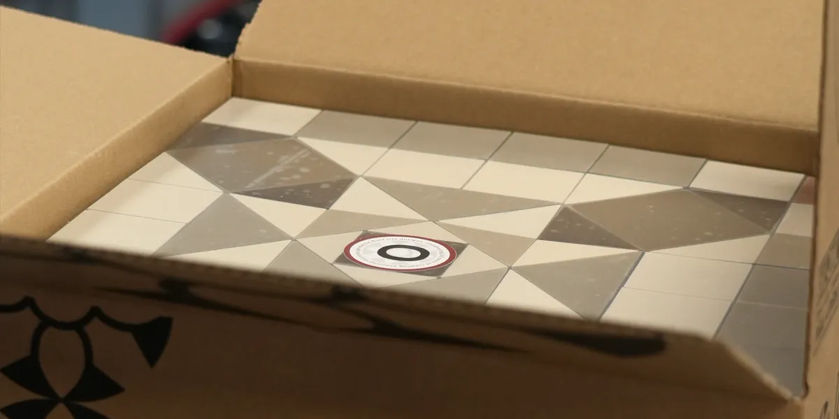 A London Mosaic branded cardboard box with grey toned sheeted mosaic tiles inside.