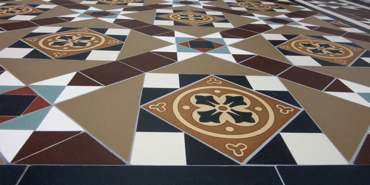 Close up view across a traditional Victorian style mosaic. The pattern is made up of mainly black, white and brown-toned tiles, and includes a large 3-colour encaustic tile.