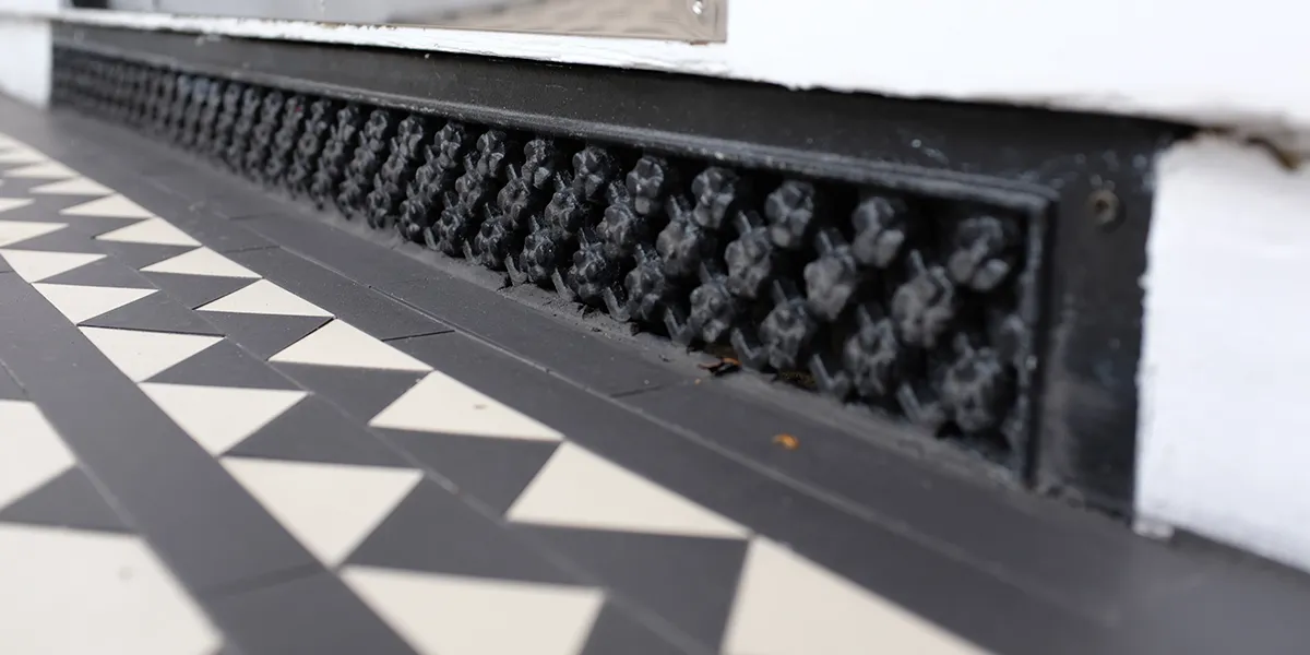 Daisy grate ventilation grille under door step, next to black and white mosaic tiles