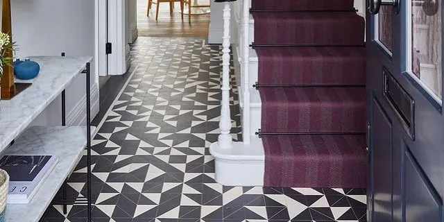 Random pattern of black and white triangle tiles on hallway floor alongside staircase with deep purple stair runner.