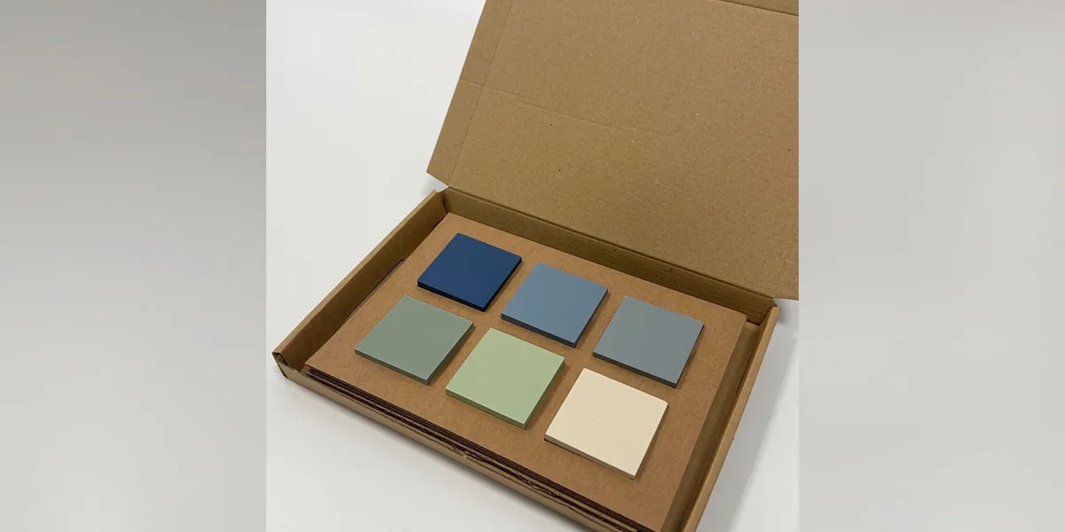 Cardboard mailing box containing 6 ceramic tile samples in blue, green and white tones.