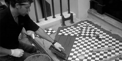 Black and white photograph of a tiler at work installing London Mosaic sheeted tiles.