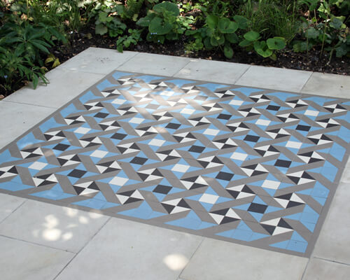 Contemporary geometric tile pattern in black, white, blue and grey as an exterior garden tile feature, surrounded with stone slabs.